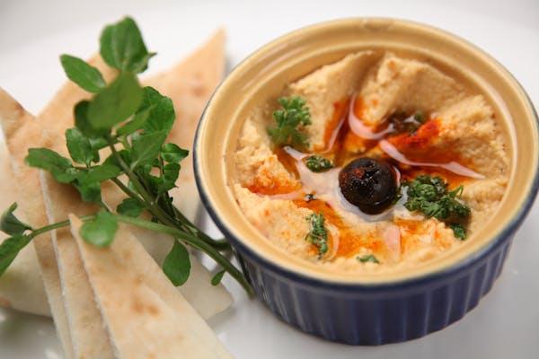 A side of hummus next to slices of pita bread
